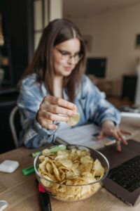 Vrouw eet chips terwijl ze thuis op haar laptop werkt, als beeld van snacken bij stress