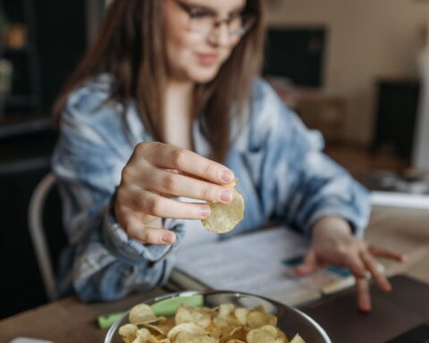 Vrouw eet chips terwijl ze thuis op haar laptop werkt, als beeld van snacken bij stress