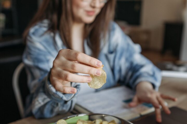 Vrouw eet chips terwijl ze thuis op haar laptop werkt, als beeld van snacken bij stress