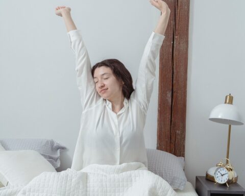Vrouw in pyjama rekt zich uit in bed terwijl het ochtendlicht de slaapkamer binnenvalt