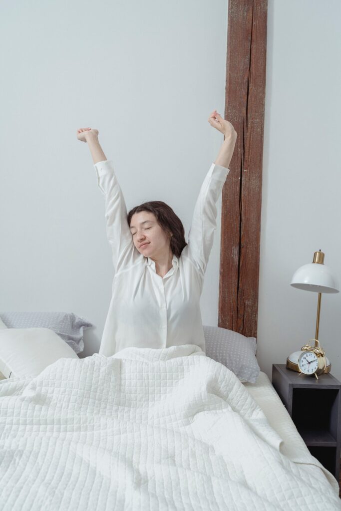 Vrouw in pyjama rekt zich uit in bed terwijl het ochtendlicht de slaapkamer binnenvalt