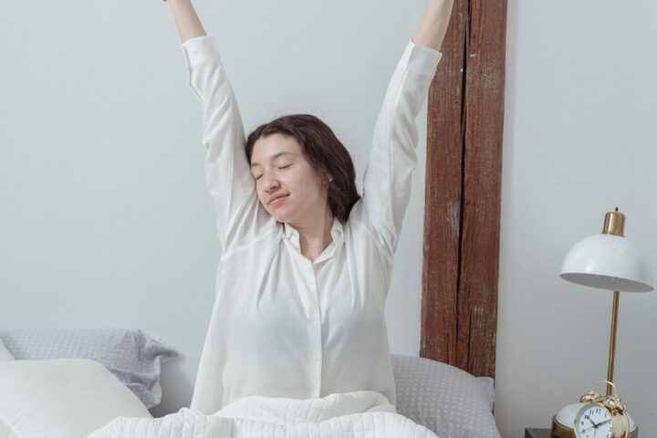 Vrouw in pyjama rekt zich uit in bed terwijl het ochtendlicht de slaapkamer binnenvalt